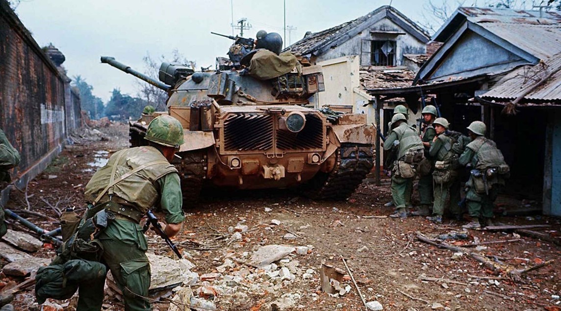 Foto van een Amerikaanse tank die met soldaten een dorpje wilt bevrijden